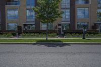 a man walking down the street past buildings with windows on them and green plants in front