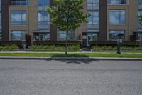 a man walking down the street past buildings with windows on them and green plants in front