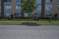 a man walking down the street past buildings with windows on them and green plants in front