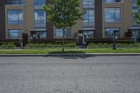 a man walking down the street past buildings with windows on them and green plants in front