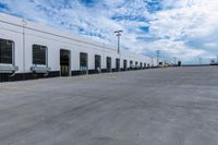 a parking lot with two doors and a white building in the back ground and the sky behind it