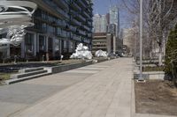 a long walkway with a white sculpture near some tall buildings and trees in the city