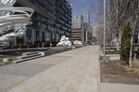 a long walkway with a white sculpture near some tall buildings and trees in the city