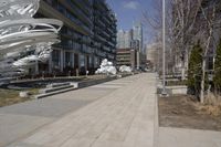 a long walkway with a white sculpture near some tall buildings and trees in the city