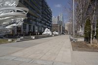 a long walkway with a white sculpture near some tall buildings and trees in the city