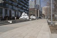 a long walkway with a white sculpture near some tall buildings and trees in the city