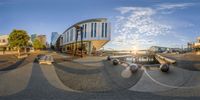 fish eye lens of buildings and benches on a city street in front of a lake