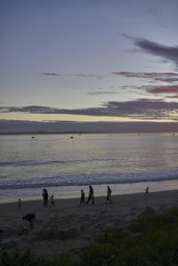 sunset with clouds and people running on a beach by the ocean with a surfer walking by