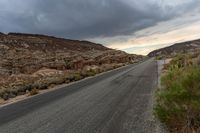 a road in the middle of a valley covered with rocky mountains under an overcast sky