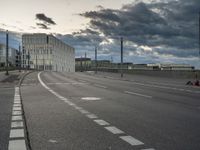 a cloudy view of an empty road between buildings with a person riding a skateboard on it