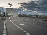 a cloudy view of an empty road between buildings with a person riding a skateboard on it