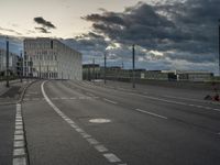 a cloudy view of an empty road between buildings with a person riding a skateboard on it