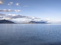 the large body of water in the open field on a sunny day, with small clouds above mountains