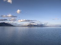 the large body of water in the open field on a sunny day, with small clouds above mountains