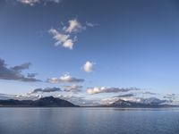 the large body of water in the open field on a sunny day, with small clouds above mountains