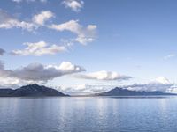 the large body of water in the open field on a sunny day, with small clouds above mountains