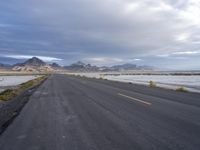 a long empty highway that has mountains in the distance, and snow in the background