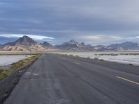 a long empty highway that has mountains in the distance, and snow in the background