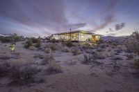 a desert house with a modern interior lit up at dusk in the evening with clouds overhead