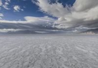 an empty desert plain, with footprints in the sand, under a cloudy sky with mountains and mountains