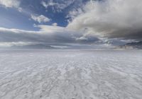 an empty desert plain, with footprints in the sand, under a cloudy sky with mountains and mountains