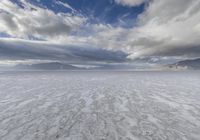 an empty desert plain, with footprints in the sand, under a cloudy sky with mountains and mountains