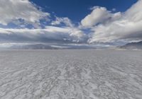 an empty desert plain, with footprints in the sand, under a cloudy sky with mountains and mountains