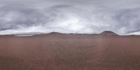 an arid desert with a few small rocks in the distance and large cloud covering the sky