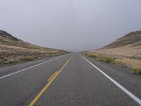 two empty roads with mountains and grass on the side on a cloudy day, with only one car