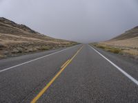 two empty roads with mountains and grass on the side on a cloudy day, with only one car