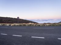 an empty winding road on a mountain with the sun set above the mountains in the background