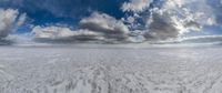 a panoramic picture of a vast white plain with footprints in the sand and fluffy clouds