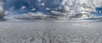 a panoramic picture of a vast white plain with footprints in the sand and fluffy clouds