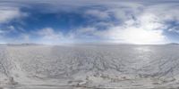 the snow - covered surface of a large field under a cloudy blue sky and the sun peeking out