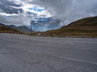 an empty street in front of the mountains with storm clouds in the sky and mountains around it