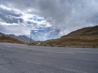 an empty street in front of the mountains with storm clouds in the sky and mountains around it