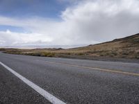 a paved road with yellow lines under cloudy skies at high speeds on a mountain road