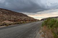 a winding, open road in a desert under stormy skies of a cloudy day with grey clouds