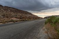 a winding, open road in a desert under stormy skies of a cloudy day with grey clouds