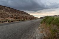 a winding, open road in a desert under stormy skies of a cloudy day with grey clouds