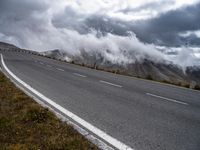 a road next to the mountains under dark clouds with steam coming from the hills on the side