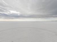 an empty field covered in white snow under a cloudy sky near the ocean in front of the horizon