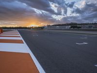 the sun sets in on an airport runway with a cloudy sky above it and some orange stripes