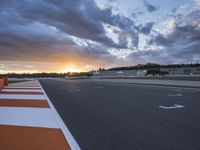 the sun sets in on an airport runway with a cloudy sky above it and some orange stripes