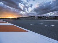 the sun sets in on an airport runway with a cloudy sky above it and some orange stripes