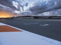 the sun sets in on an airport runway with a cloudy sky above it and some orange stripes