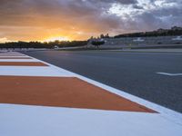 the sun sets in on an airport runway with a cloudy sky above it and some orange stripes