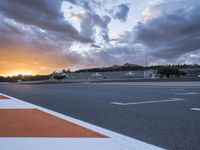 the sun sets in on an airport runway with a cloudy sky above it and some orange stripes