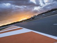 the sun sets in on an airport runway with a cloudy sky above it and some orange stripes