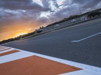 the sun sets in on an airport runway with a cloudy sky above it and some orange stripes